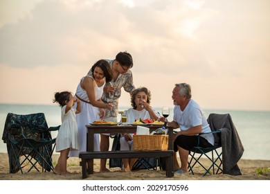 Happy Asian family on holiday vacation. Group of multi generation family little girl with parents and grandparents relax and enjoy with dinner party and dancing together on the beach at summer sunset. - Powered by Shutterstock