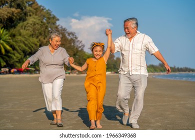 Happy Asian Family On Summer Travel Vacation. Grandfather And Grandmother Walking Together With Grandchild Girl On The Beach. Senior Couple With Granddaughter Enjoy And Having Fun Outdoor Lifestyle.