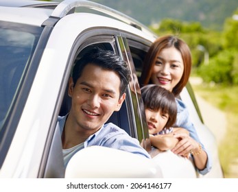 Happy Asian Family With One Child Sticking Head Out Of Car Window While Traveling On Road