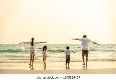 Happy Asian Family Parents With Two Child Boy And Girl Holding Hands And Walking Together On The Beach At Summer Sunset. Father, Mother And Kids Enjoy And Having Fun In Outdoor Holiday Vacation.