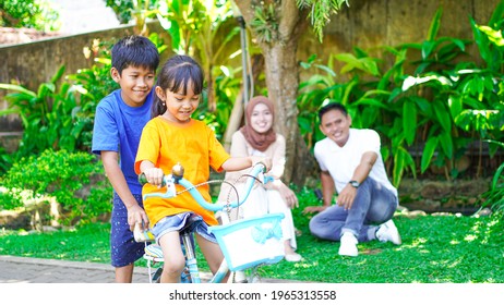 Happy Asian Family Playing Bike Together In The Park