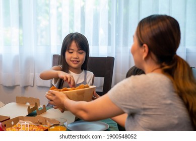 Happy Asian Family Relationship At Home. Mother With Little Daughter And Son Eating Fried Chicken And Pizza On The Table.  