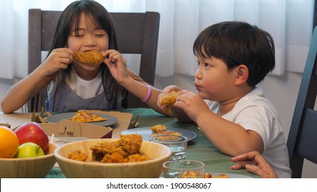 Happy Asian Family Relationship At Home. Mother With Little Daughter And Son Eating Fried Chicken And Pizza On The Table. Parents With Two Child Kids Enjoy And Having Fun With Lunch Together At Home.