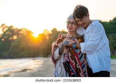 Happy Asian family senior couple enjoy outdoor lifestyle at the beach on summer holiday vacation. Senior man husband cover his wife with a blanket and hugging together on the beach at summer sunset - Powered by Shutterstock