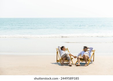 Happy Asian family senior couple enjoy outdoor lifestyle on summer beach holiday vacation at the sea. Elderly retired man and woman relaxing on beach chair and holding hands together at summer sunset - Powered by Shutterstock