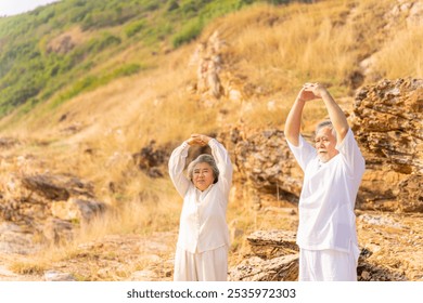 Happy Asian family senior couple practicing yoga and meditation on rocky coastal hill at sunset. Healthy elderly people enjoy wellness and outdoor lifestyle. Mental health care and motivation concept. - Powered by Shutterstock