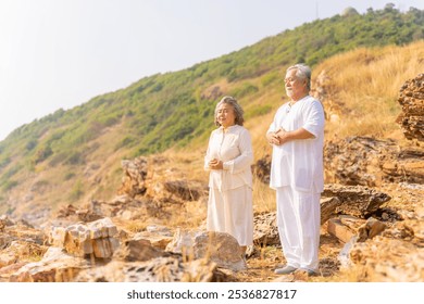 Happy Asian family senior couple practicing yoga and meditation on rocky coastal hill at sunset. Healthy elderly people enjoy wellness and outdoor lifestyle. Mental health care and motivation concept. - Powered by Shutterstock