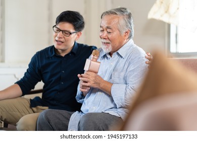 Happy Asian Family. Senior Asian Father And Adult Son Singing Karaoke On The Sofa In The Living Room At Home. Home Entertainment.