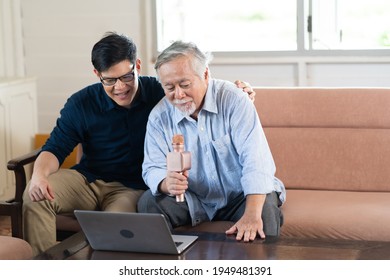 Happy Asian Family. Senior Asian Father And Adult Son Singing Karaoke On The Sofa In The Living Room At Home. Home Entertainment.