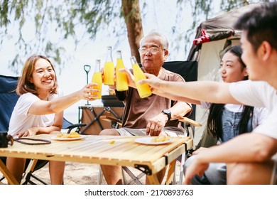 Happy Asian Family With A Senior Grandfather Cheers Orange Juice Together During Picnic And Camping On Tropical Beach. Summer Activity. Relax And Outdoor Activity Lifestyle Family Concept