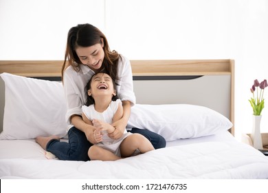 Happy Asian Family. Single Mother And Kid Daughter Aged Three Playing Together On The Bed In The House With Sunlight From The Window.