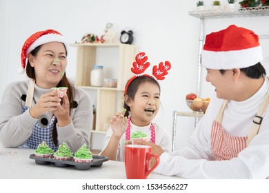 Happy Asian Family Sitting At Kitchen  Holding And Eating Cup Cake Together Christmas Day.