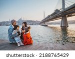 happy asian family sitting on the side of bosphorus looking at beautiful sunset in istanbul turkey