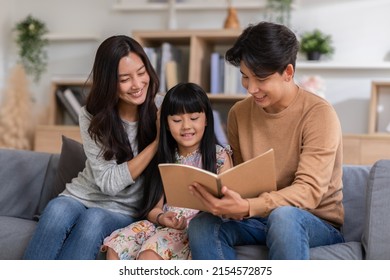 Happy Asian family sitting on the sofa together looking at daughter's note book. Parents are smiling, reading daughter book and proud of education progress. Watching book together, family relationship - Powered by Shutterstock