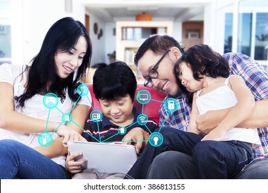 Happy Asian Family Sitting On The Sofa While Using A Digital Tablet With Smart Home System Controller
