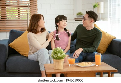 Happy Asian Family Sitting Together On Sofa At Home Living Room.