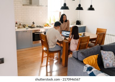 Happy Asian Family Sitting Together On Cozy Kitchen At Home. Father Working With Laptop