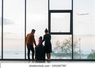 Happy Asian Family With Suitcases In The Airport. Little Boy Sitting On Suitcase While Father And Mother Standing Near Window At The Airport And Watching Plane Before Departure On Vacation.