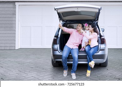 Happy Asian Family Taking Selfie Photo Together With A Smartphone While Sitting In The Open Car Baggage