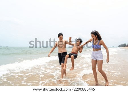 Happy Asian family travel ocean on summer holiday vacation. Parents and little son in swimwear have fun outdoor activity lifestyle walking and playing sea water together at tropical beach in sunny day