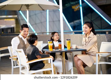 Happy Asian Family With Two Children Relaxing Talking Having Drinks And Desserts At An Outdoor Coffee Place.