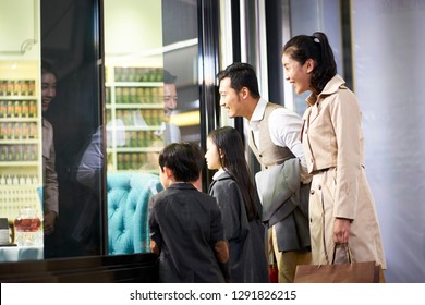 Happy Asian Family With Two Children Looking Into A Shop Window In Shopping Mall