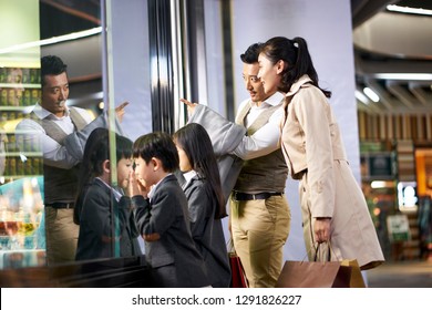 Happy Asian Family With Two Children Looking Into A Shop Window In Shopping Mall