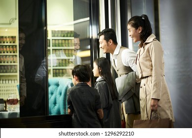 Happy Asian Family With Two Children Looking Into A Shop Window In Shopping Mall