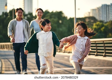 happy asian family and two children walking pedestrian bridge in city park