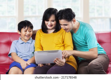 Happy Asian Family Using Digital Tablet On Couch, Shot At Home