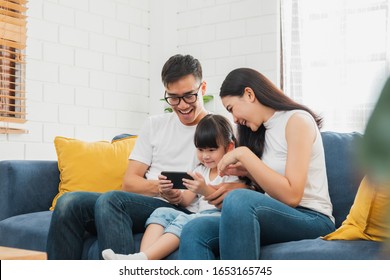 Happy Asian Family Using Tablet, Laptop, Phone For Playing Game Watching Movies, Relaxing At Home For Technology Lifestyle Concept