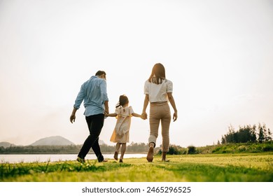 Happy Asian family walking and playing together in a beautiful nature setting, with green grass and a sunny background, on a summer day, Family day, back view - Powered by Shutterstock