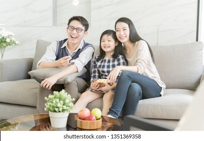 Happy Asian Family Watching Tv Together On Sofa In Living Room. Family And Home Concept