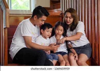 Happy Asian Family Watching Video On Mobile Phone At Home Together. Father,mother ,son,daughter Using Smartphones On Stair. Parents And Children                               