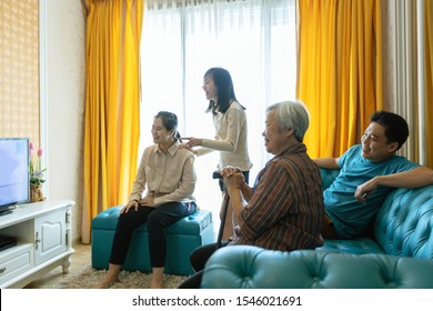 Happy asian family,father,mother,daughter,and senior grandmother relaxing,watching movies dramas series on TV,enjoying watch television and laughing in living room at home,lifestyle,weekend activities