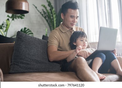 Happy Asian Father And Daughter Looking At The Laptop At Home.