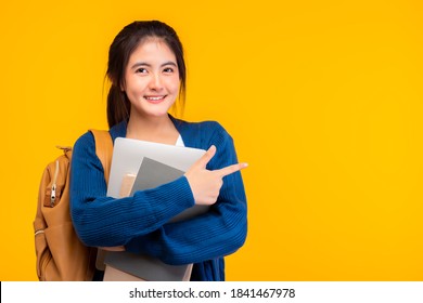 Happy Asian Female College Student Smiling At Camera On Yellow Background, Holding Tablet And Books, Hanging Bag Pack. Youth Girl Student Pointing Up To Copy Space. Education Exchange Student Concept