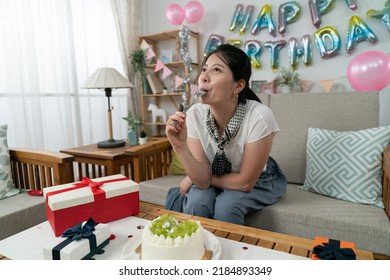 happy asian female licking cream and keeping spoon in mouth while enjoying tasty cake by herself at her birthday party in the apartment with celebration decors. - Powered by Shutterstock