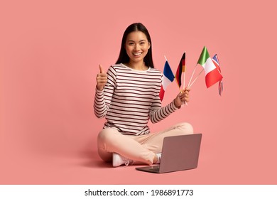 Happy Asian Female Sitting With International Flags And Laptop And Showing Thumb Up, Positive Millennial Korean Student Woman Recommending Website For Learning Foreign Languages Online, Copy Space