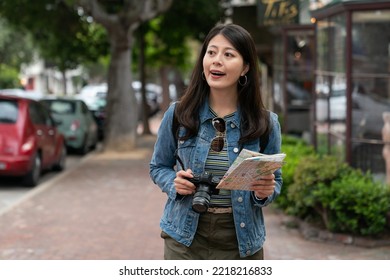 Happy Asian Female Tourist Having Fun Exploring The Charming Beach Town Carmel By The Sea With Camera And City Map. She Looks Around Her Surroundings While Taking Stroll On Street