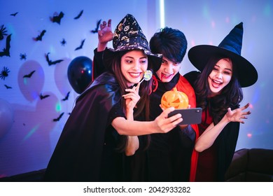 Happy Asian Friends Using Smartphone Taking Selfie In Halloween Night Party. Group Of Young Smiling People Enjoying And Celebrating Halloween At Home Or Nightclub.