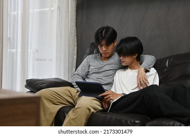 Happy Asian Gay Couple Having A Good Moment And Spending The Day Together In Their Home While They Using A Tablet, LGBT Couples And Everyday Life At Home Concept.