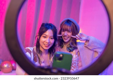 Happy Asian generation z woman friends vlogger influencer content creator enjoy and fun using smartphone online live streaming viral video cover dance on social media application in bedroom at home.