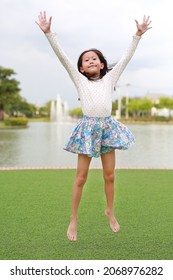 Happy Asian Girl Child Jumping In The Garden Outdoor.