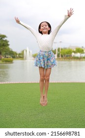 Happy Asian Girl Child Jumping In The Garden Outdoor.