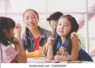 Happy Asian girl is holding a color pencil and smile drawing in kindergarten art classroom. Kid art club activity for play and learn development .concept