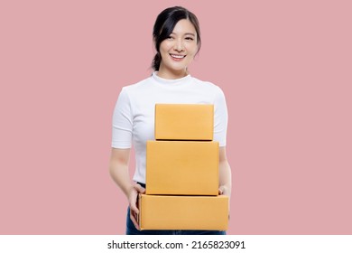 Happy Asian Girl Holding Package Parcel Boxs Isolated On Pink Screen Background. Delivery Courier And Shipping Service Concept.