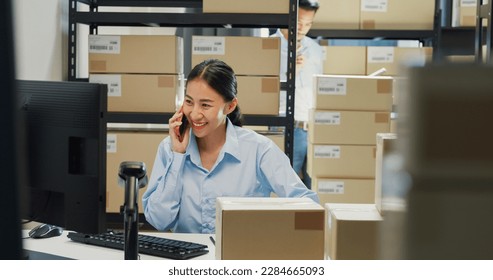 Happy Asian girl and man partner wear formal shirt sit in front desk computer pick up phone purchase order stock detail customer online data delivery at warehouse. Startup small business concept. - Powered by Shutterstock