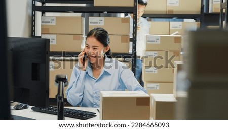 Happy Asian girl and man partner wear formal shirt sit in front desk computer pick up phone purchase order stock detail customer online data delivery at warehouse. Startup small business concept.