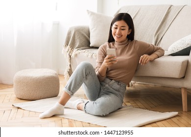 Happy Asian Girl Messaging on Phone at Home, Sitting on Floor near Sofa